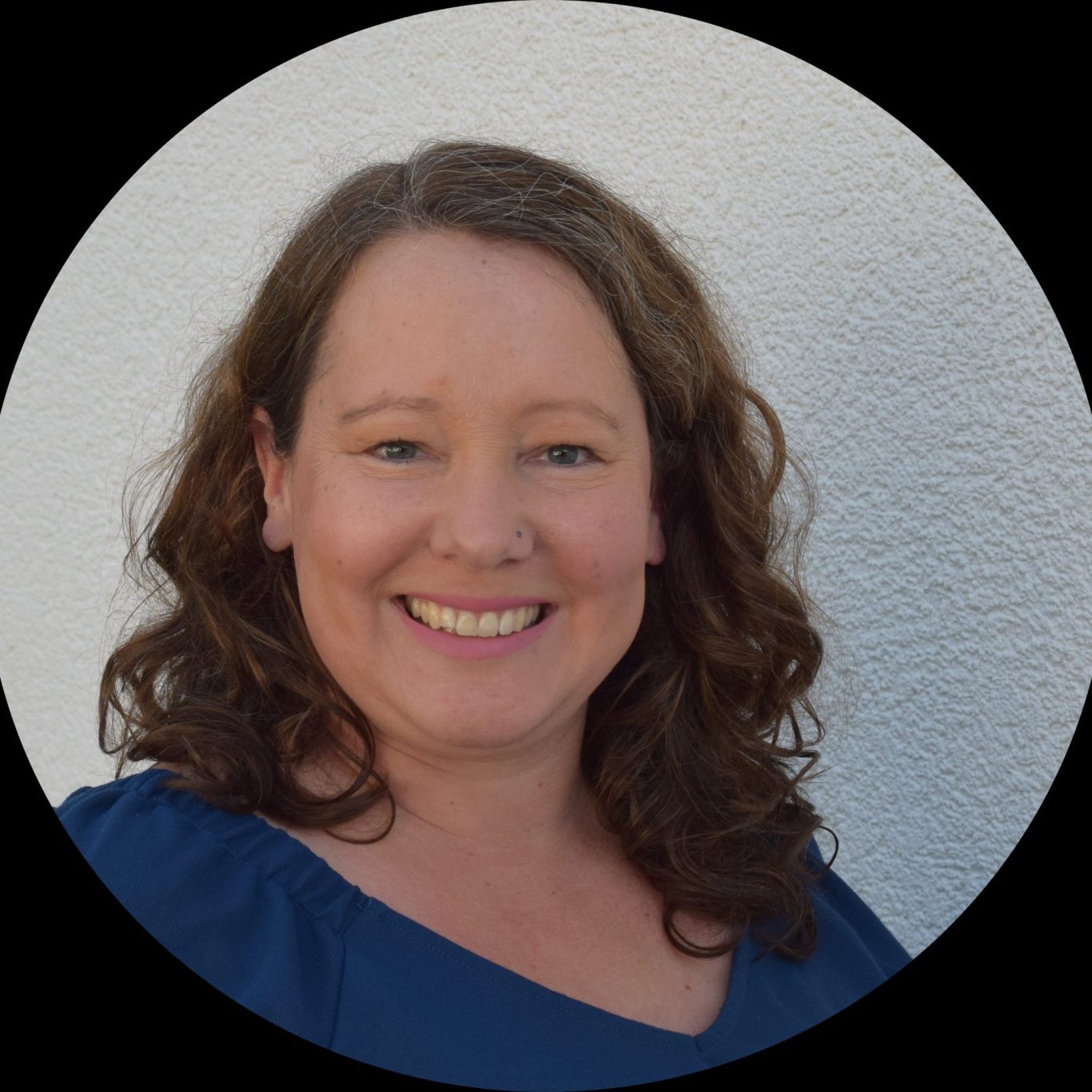 Systemische Beraterin & Coach - Kempen und am Niederrhein Porträt einer lächelnden Frau mit lockigem braunem Haar vor einem einfarbigen Hintergrund.