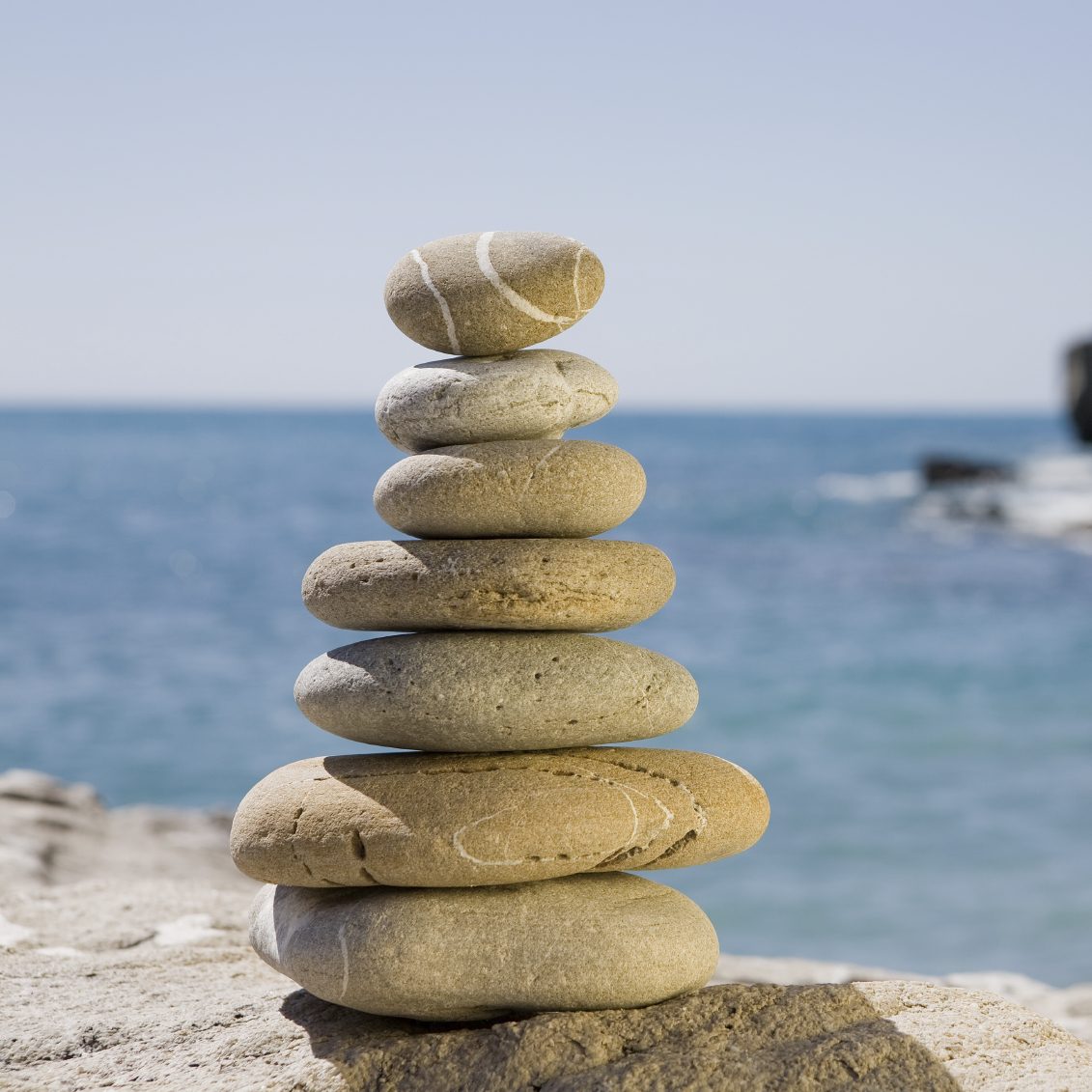 Systemische Beratung & Coachin in Kempen und am Niederrhein Ein Turm aus flachen Steinen steht am Ufer eines ruhigen Meeres.